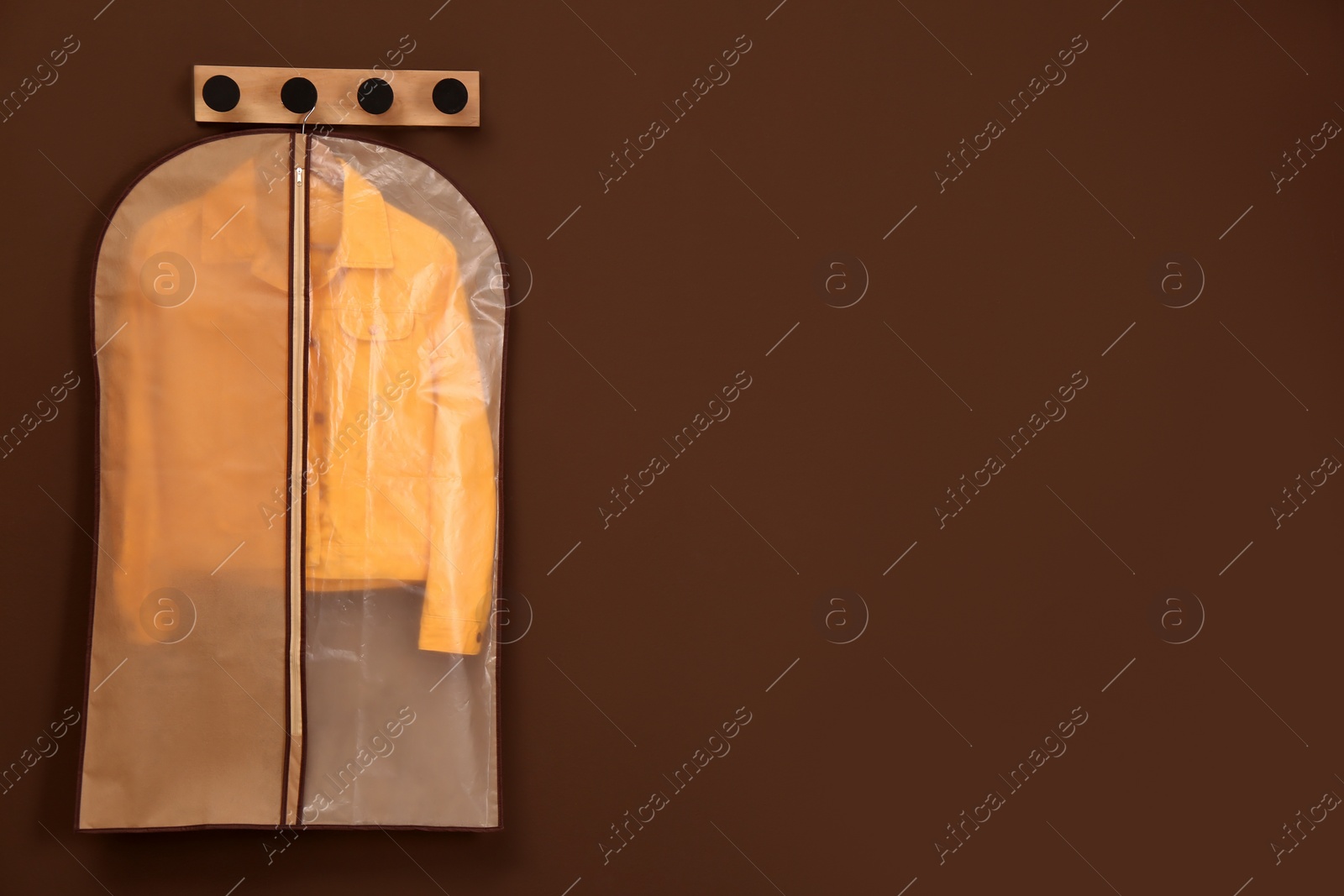 Photo of Garment bag with jacket hanging on brown wall. Space for text