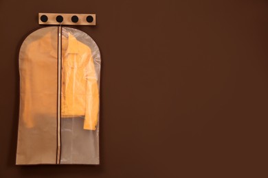 Garment bag with jacket hanging on brown wall. Space for text
