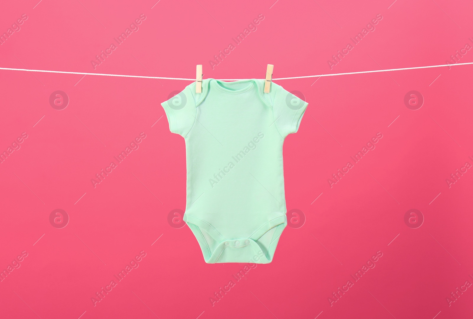Photo of Baby onesie hanging on clothes line against pink background