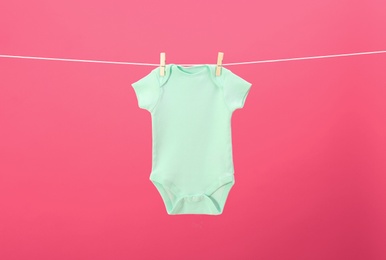 Photo of Baby onesie hanging on clothes line against pink background