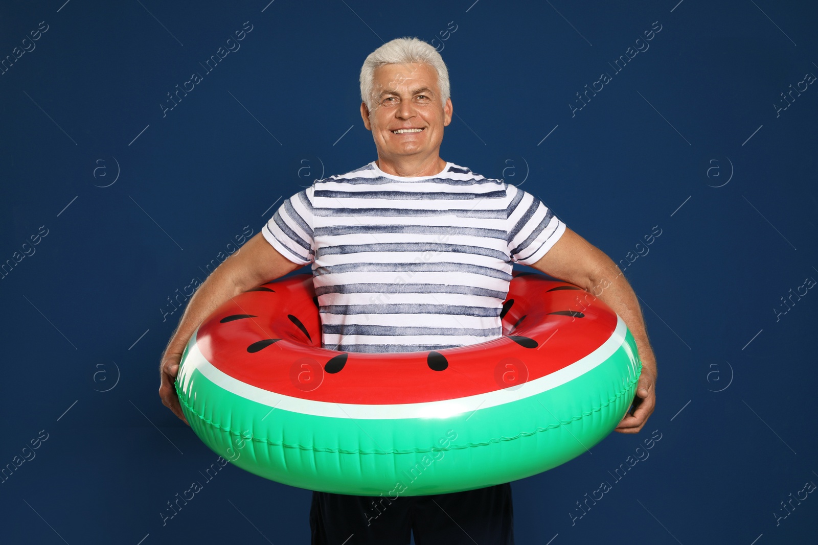 Photo of Funny mature man with bright inflatable ring on dark blue background