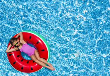 Image of Cute little girl with inflatable ring in swimming pool, top view. Space for text 