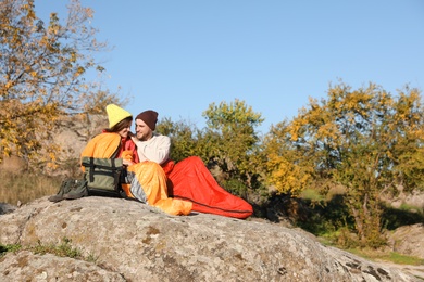 Photo of Couple of campers in sleeping bags sitting on rock. Space for text