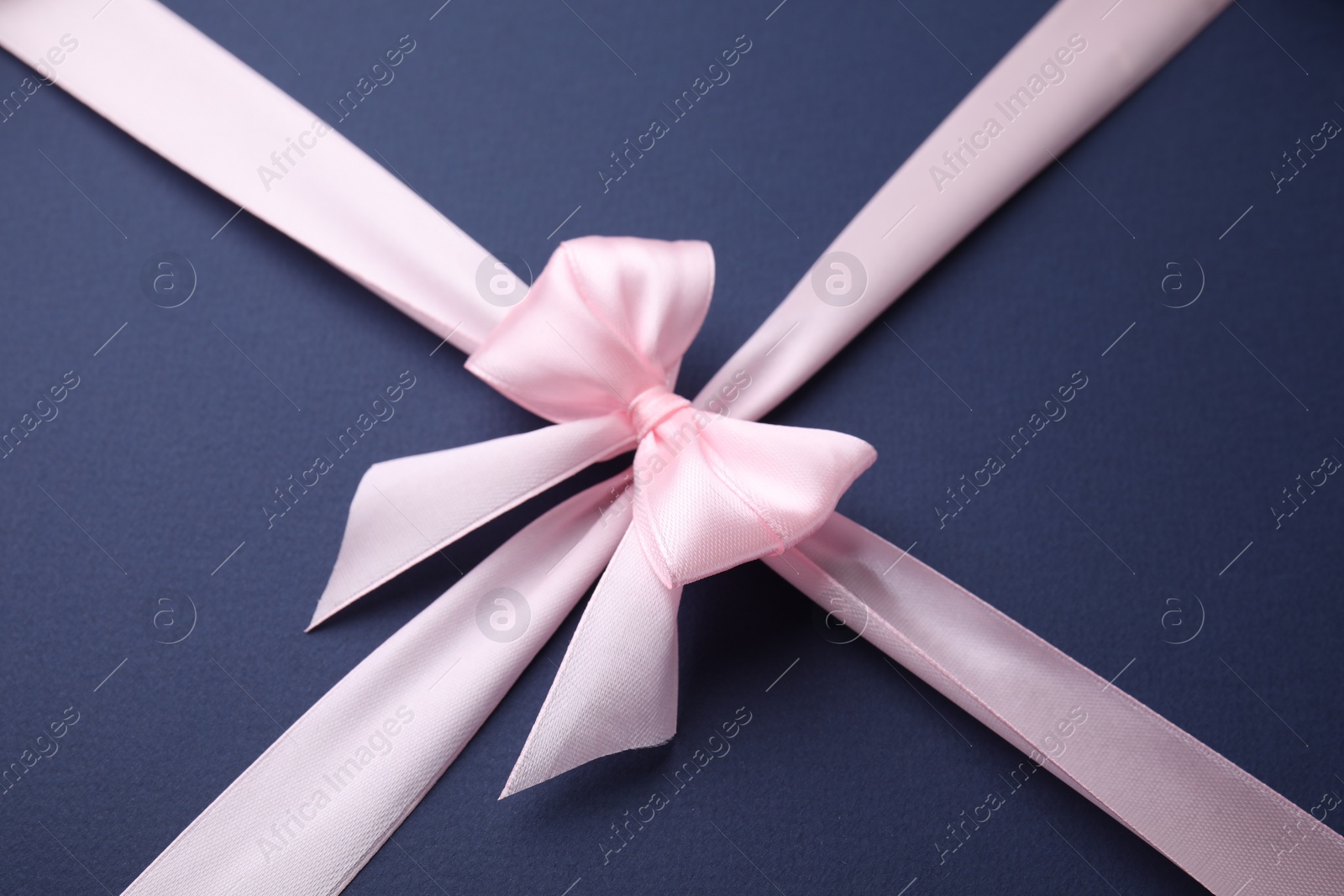 Photo of Pink satin ribbon with bow on blue background