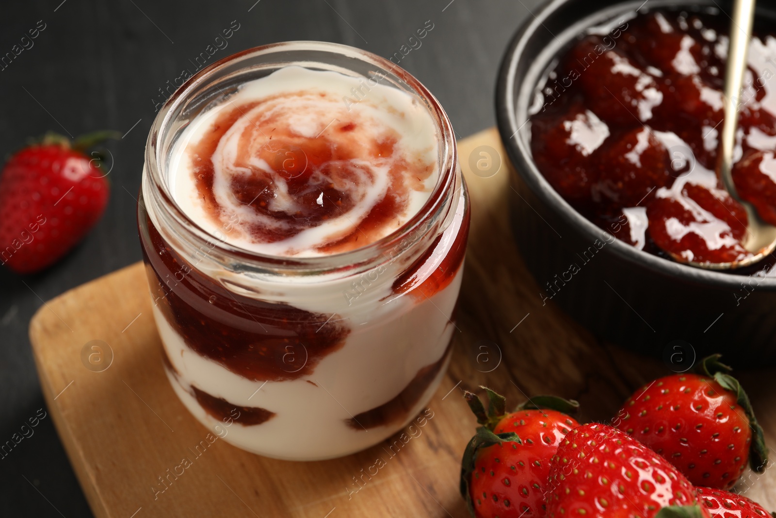 Photo of Tasty yoghurt with jam and strawberries on black table, closeup