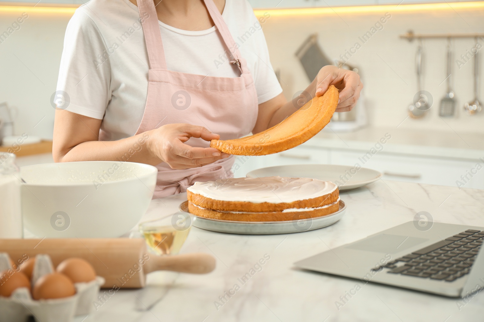 Photo of Woman making cake while watching online cooking course via laptop in kitchen, closeup
