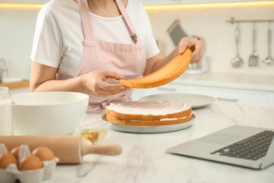Photo of Woman making cake while watching online cooking course via laptop in kitchen, closeup
