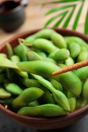 Photo of Taking edamame beans in pod from bowl with chopsticks, closeup