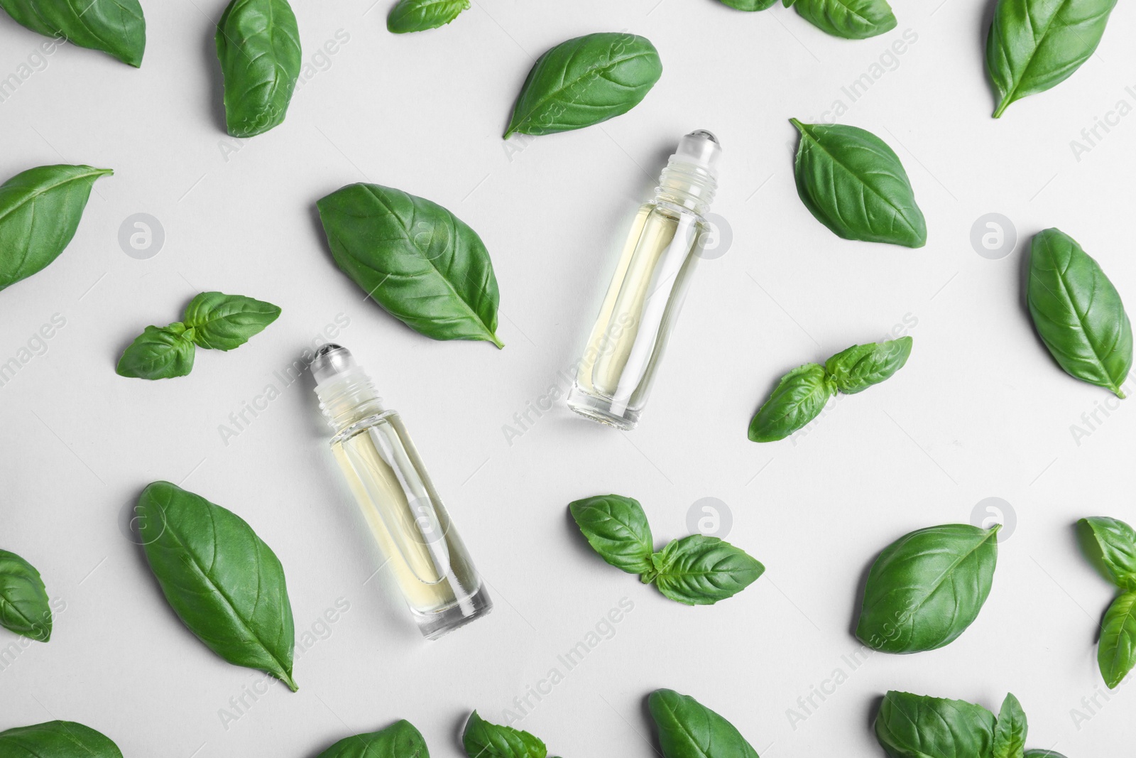 Photo of Glass bottles with essential oil among basil leaves on light background, flat lay