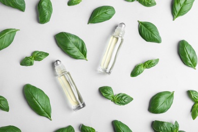 Glass bottles with essential oil among basil leaves on light background, flat lay