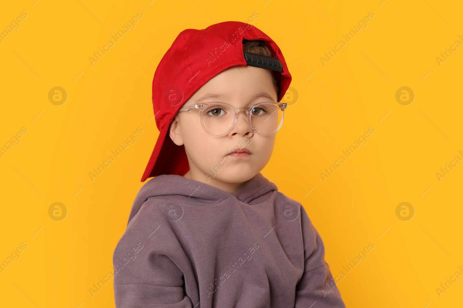 Photo of Cute little boy in glasses on orange background