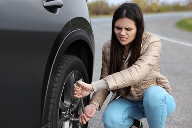 Worried young woman changing tire of car on roadside