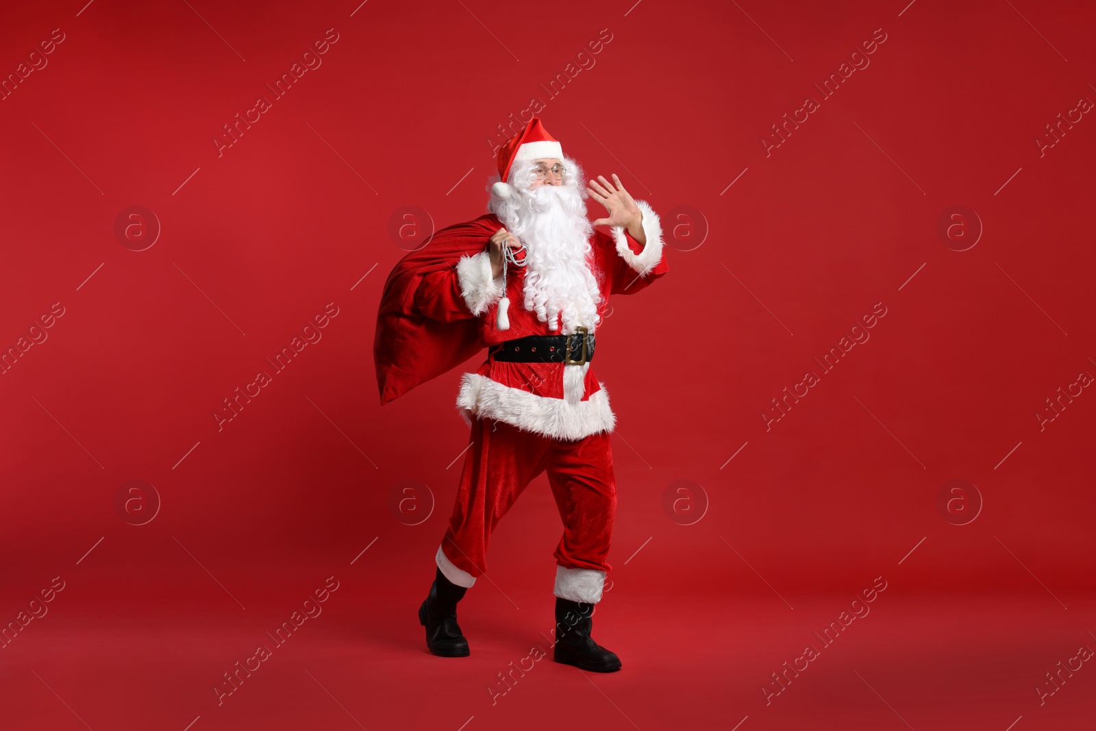 Photo of Santa Claus with bag of Christmas presents posing on red background