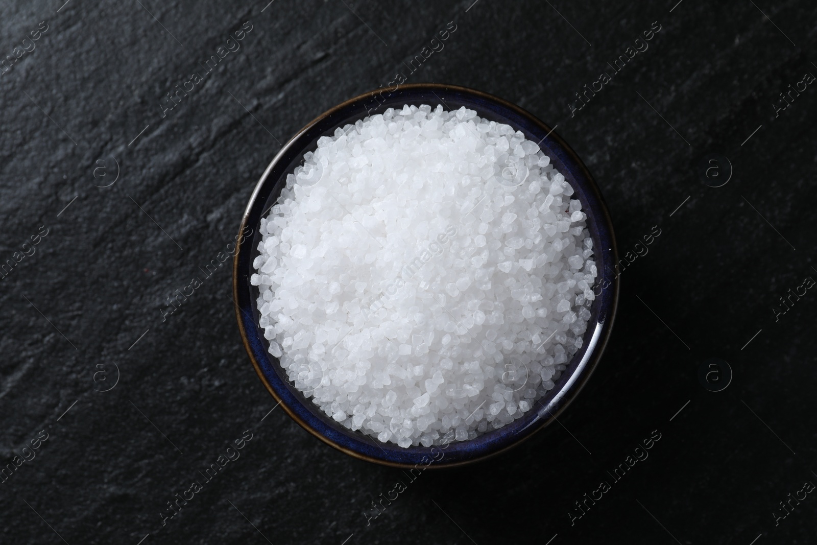 Photo of Organic white salt in bowl on black table, top view