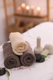 Photo of Spa stones, rolled towels and herbal bags on massage table indoors