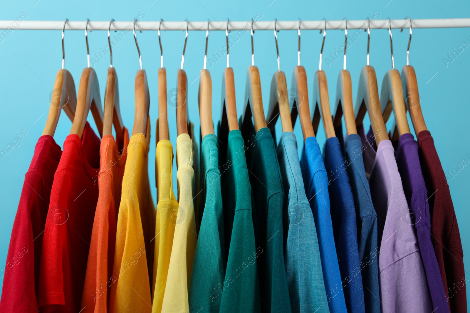 Photo of Rack with bright clothes on blue background. Rainbow colors