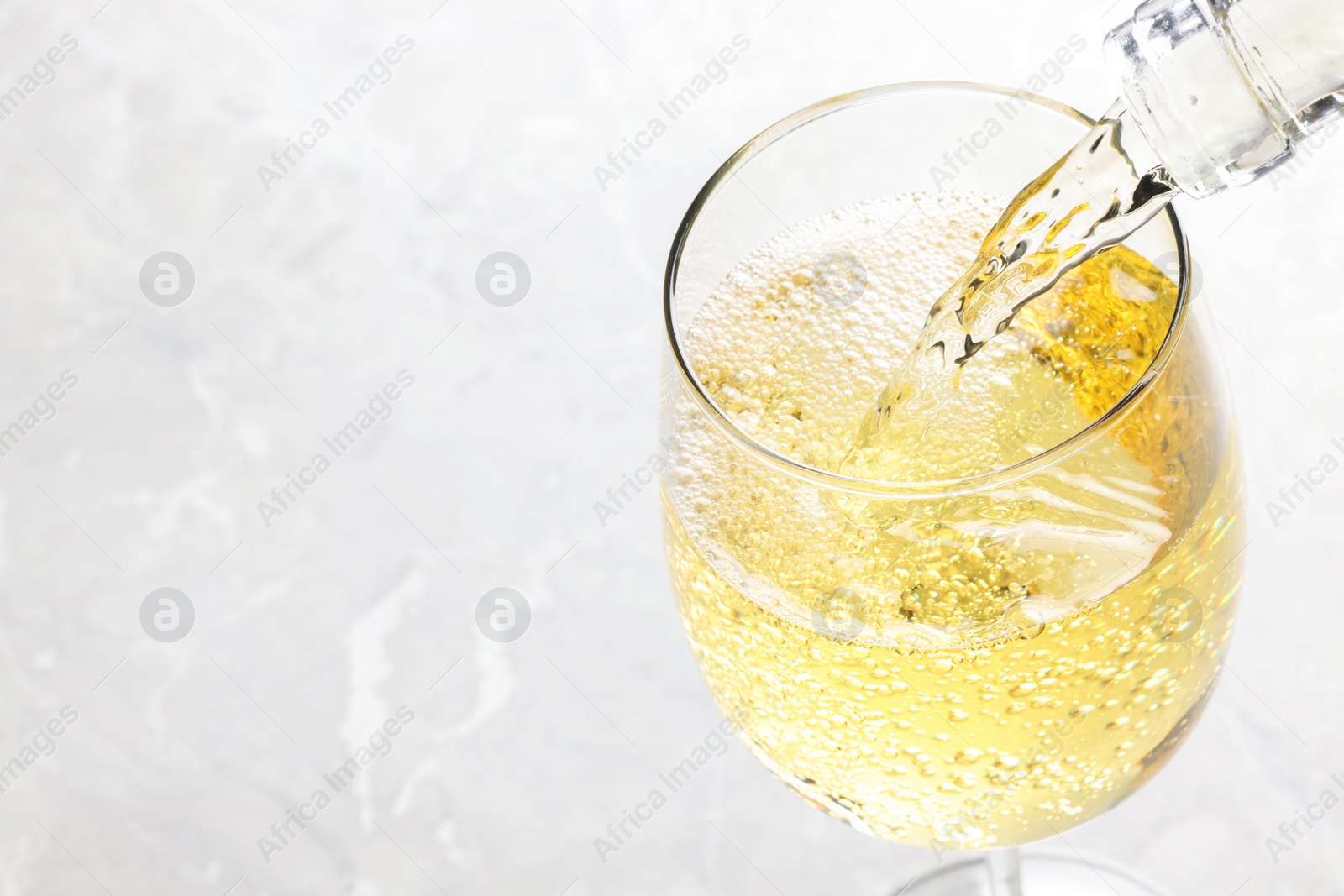 Photo of Pouring tasty aromatic wine in glass at gray marble table, closeup. Space for text