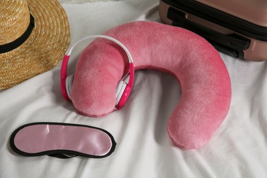 Pink travel pillow with headphones, suitcase, hat and sleep mask on bed