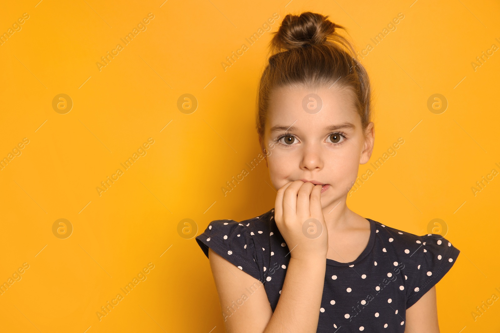 Photo of Cute little girl biting her nails on orange background, space for text