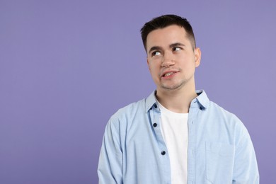 Photo of Portrait of embarrassed young man on violet background, space for text