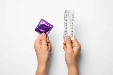 Photo of Woman holding condom and birth control pills on white background, top view. Safe sex