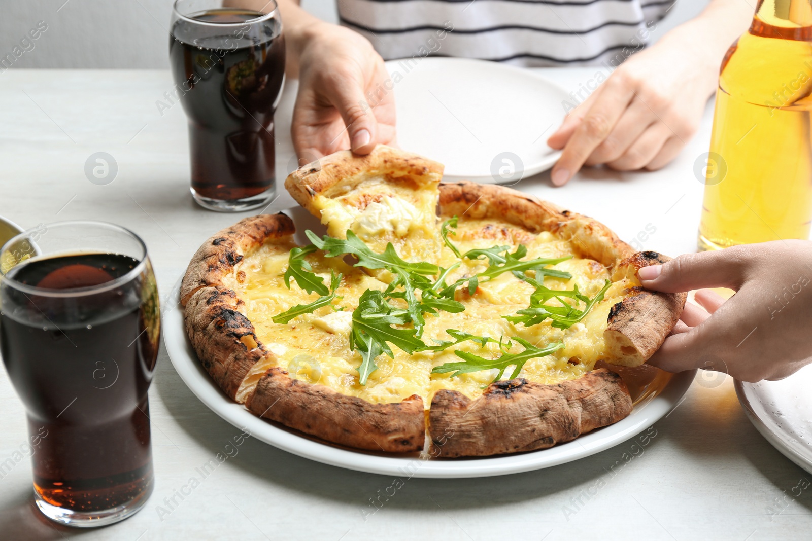 Photo of People taking pieces of delicious cheese pizza at white table, closeup