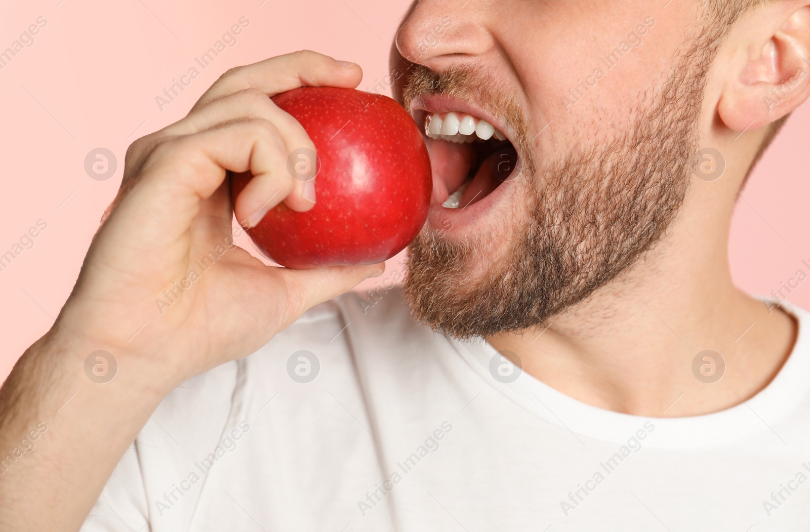 Photo of Young man with healthy teeth and apple on color background, closeup