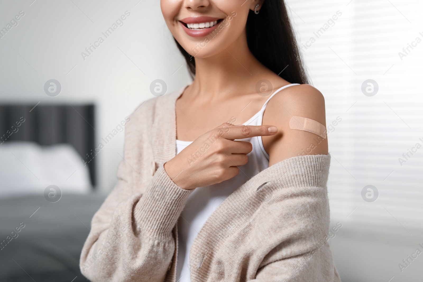 Photo of Woman pointing at sticking plaster after vaccination on her arm in bedroom, closeup