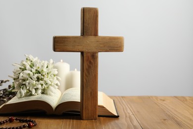 Photo of Cross, Bible, rosary beads, flowers and church candles on wooden table against light background. Space for text