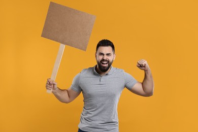 Photo of Angry man holding blank sign on orange background, space for text