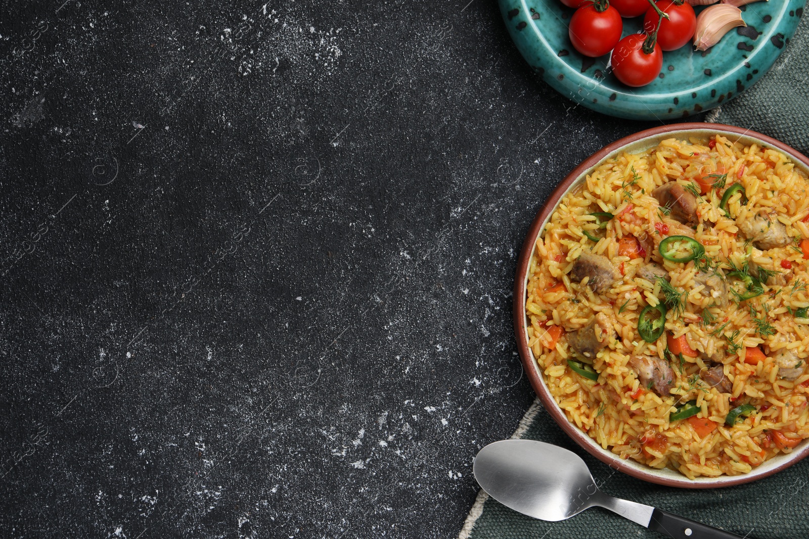 Photo of Delicious pilaf with meat and ingredients on black textured table, flat lay. Space for text