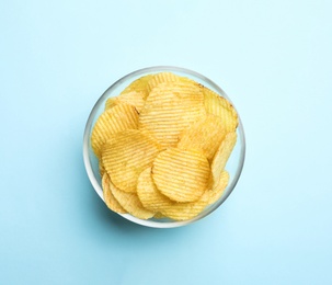 Delicious crispy potato chips in bowl on color background, top view