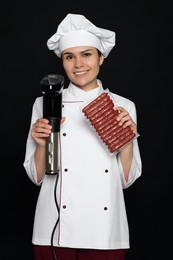 Photo of Chef holding sous vide cooker and sausages in vacuum pack on black background