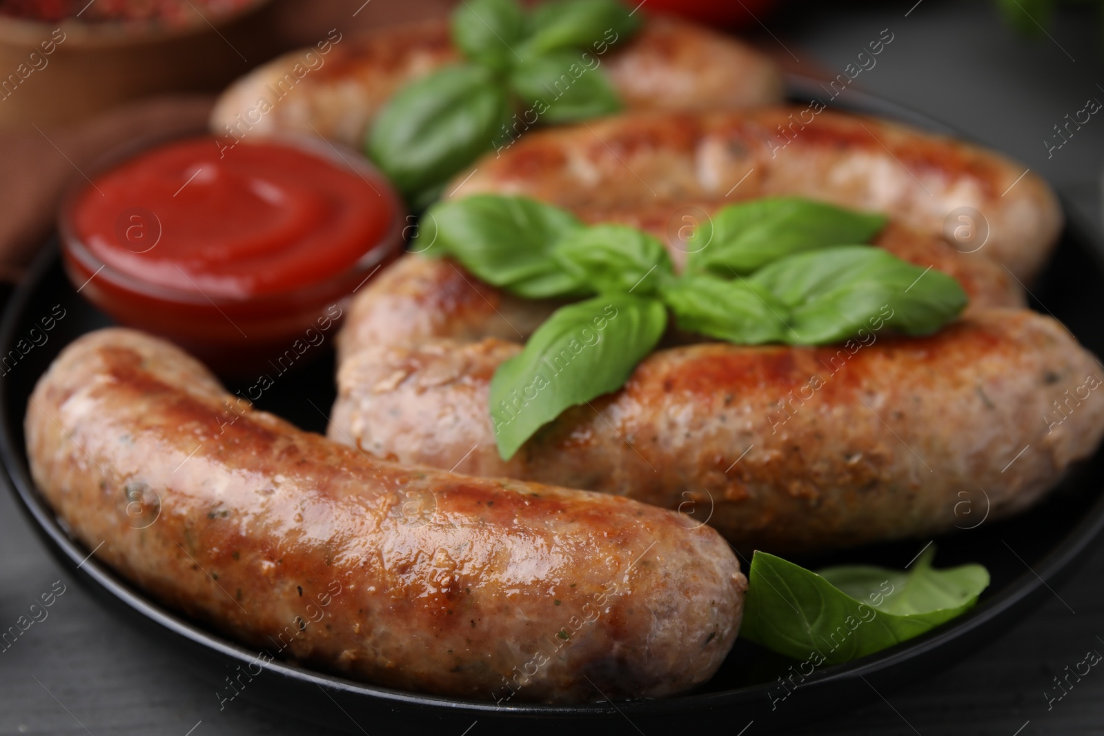 Photo of Tasty homemade sausages, ketchup and basil leaves on grey table, closeup