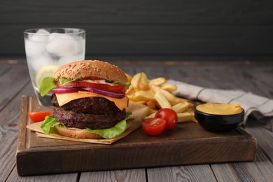 Photo of Tasty cheeseburger with patties, French fries, sauce and tomatoes on wooden table