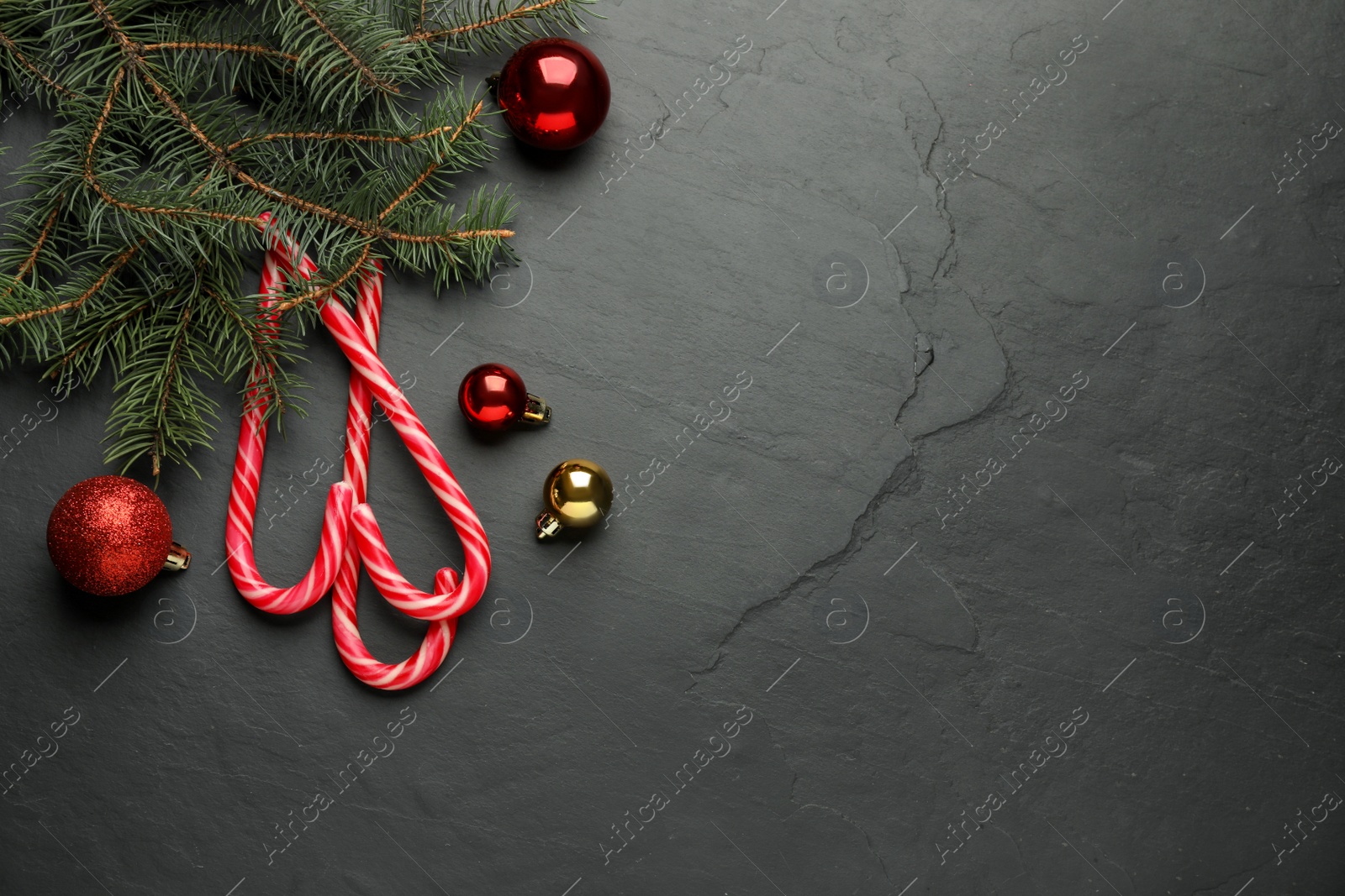 Photo of Tasty candy canes, fir branches and Christmas balls on black table, flat lay. Space for text