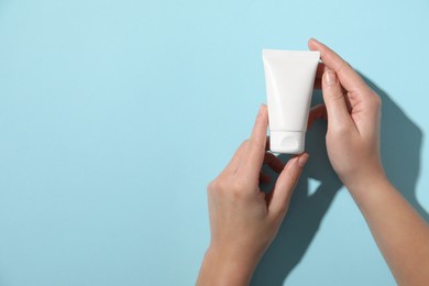 Woman with tube of hand cream on light blue background, top view. Space for text