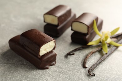 Photo of Glazed curd cheese bars, vanilla pods and flower on grey table, closeup