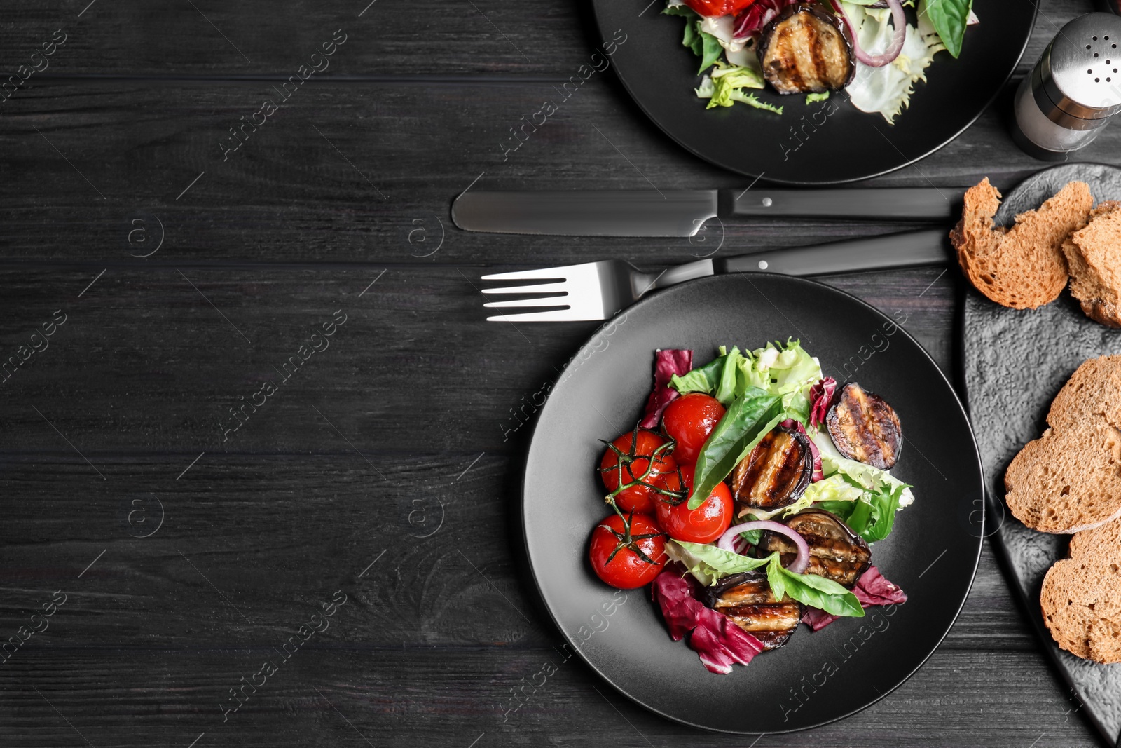 Photo of Delicious salad with roasted eggplant and basil served on black wooden table, flat lay. Space for text