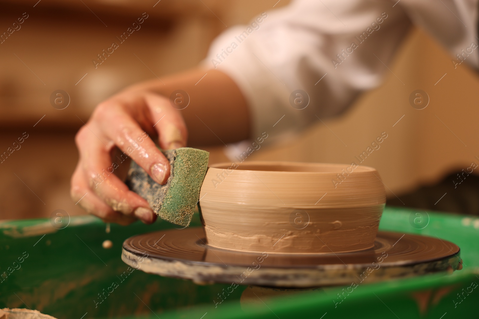 Photo of Clay crafting. Woman making bowl on potter's wheel indoors, closeup