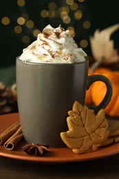 Tasty pumpkin spice latte with whipped cream in cup and cookies on table, closeup