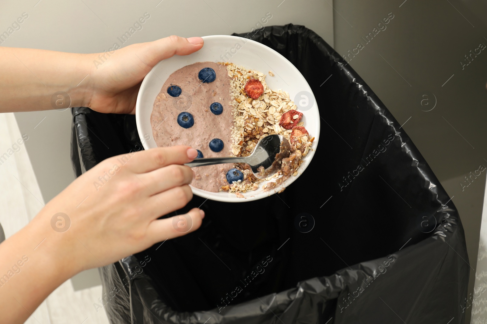 Photo of Woman throwing oatmeal with berries into bin indoors, closeup