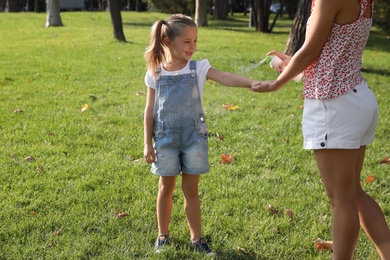 Photo of Mother applying insect repellent onto girl's hand in park