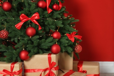 Photo of Decorated Christmas tree and gift boxes near red wall