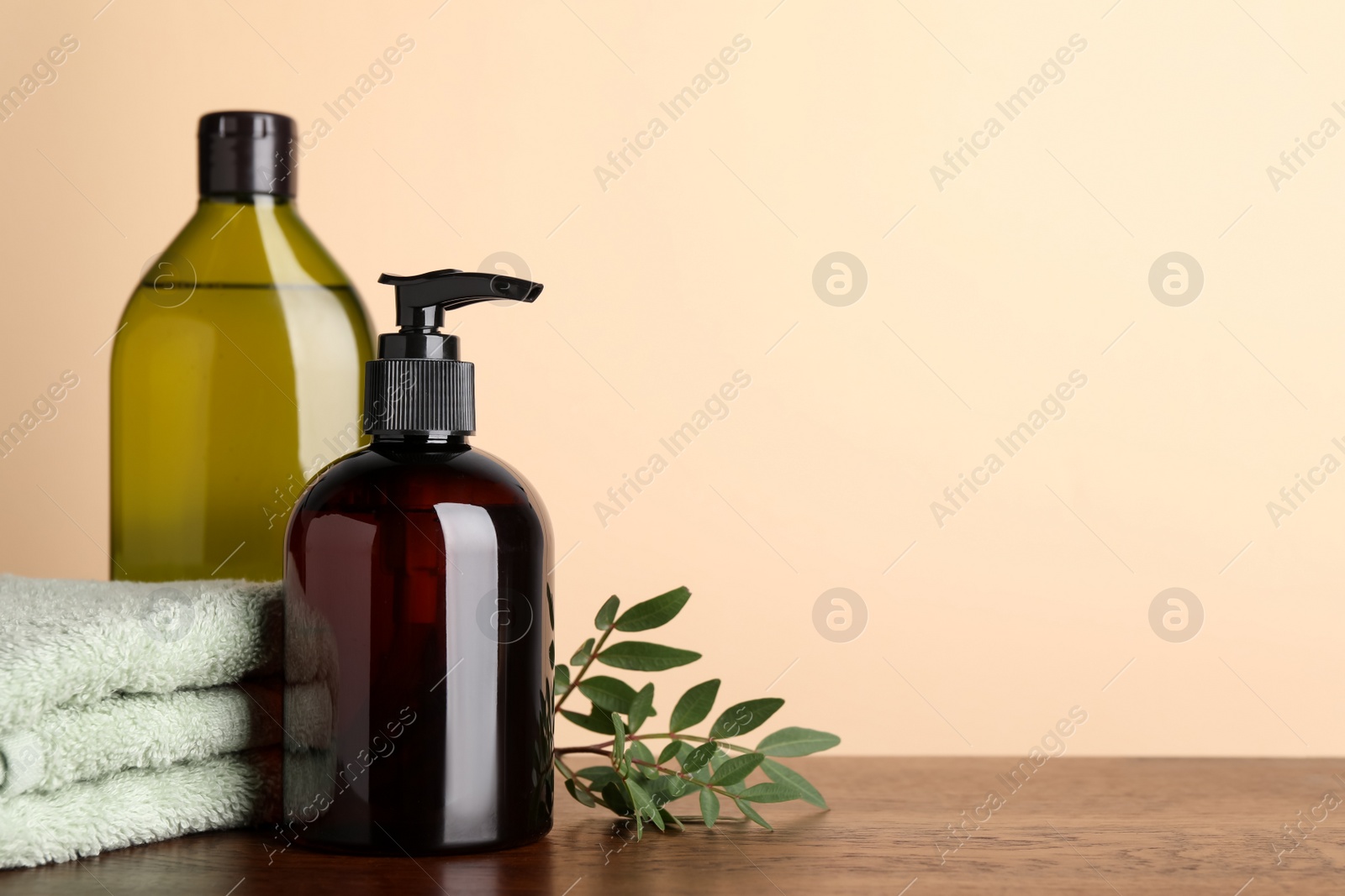 Photo of Bottles of shampoo and stacked towel on wooden table near beige wall, space for text