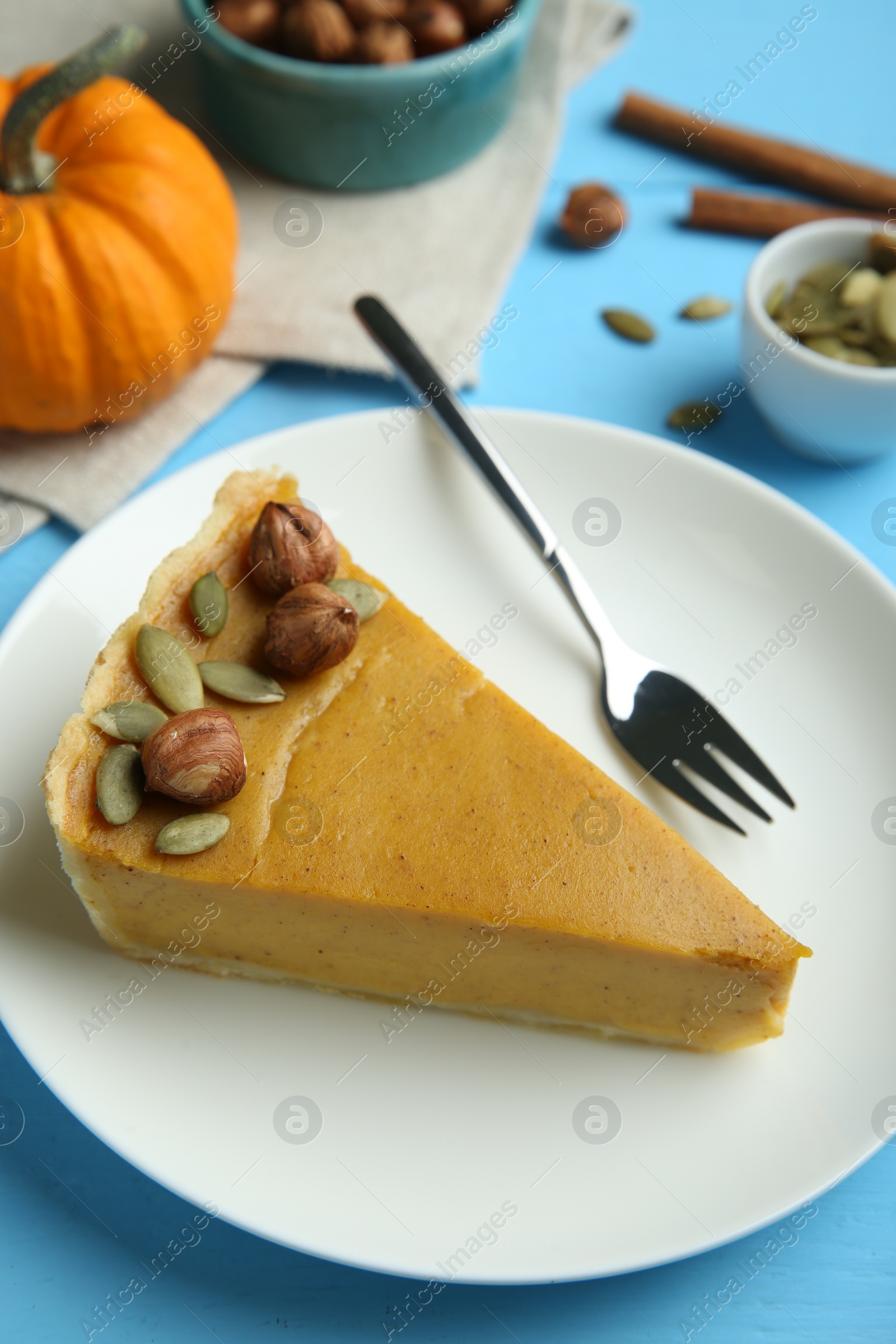 Photo of Piece of delicious pumpkin pie with hazelnuts, seeds and fork on light blue wooden table, above view