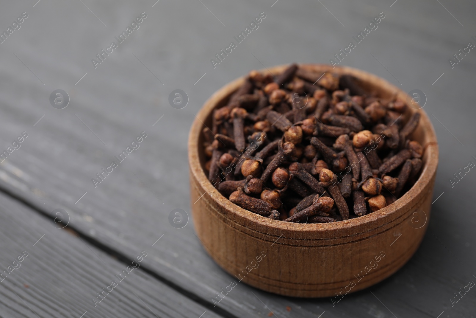 Photo of Aromatic cloves in bowl on grey wooden table, closeup. Space for text