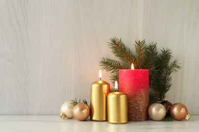 Burning candles with Christmas baubles and fir tree branch on table against wooden background. Space for text