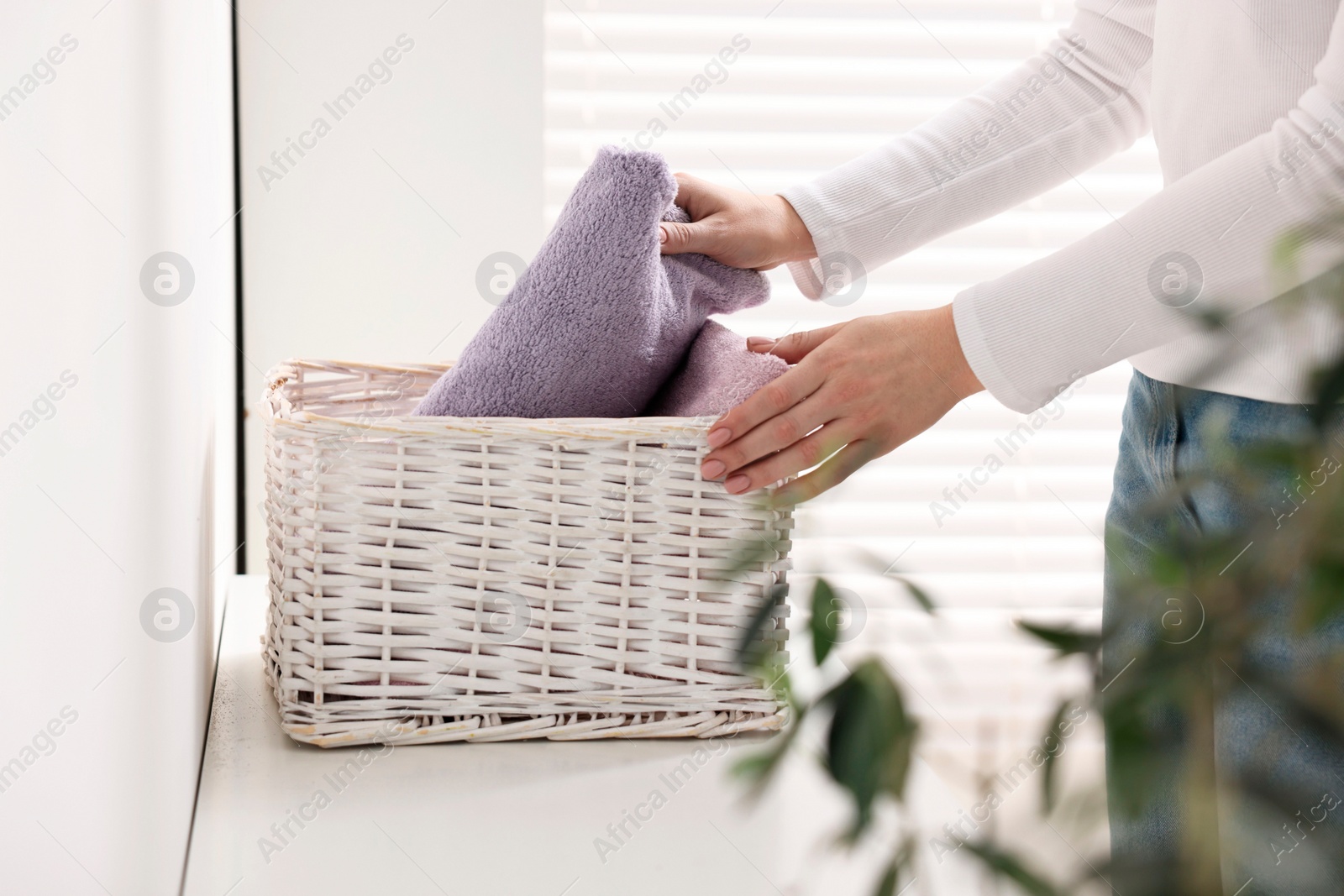 Photo of Woman with laundry basket of clean towels indoors, closeup