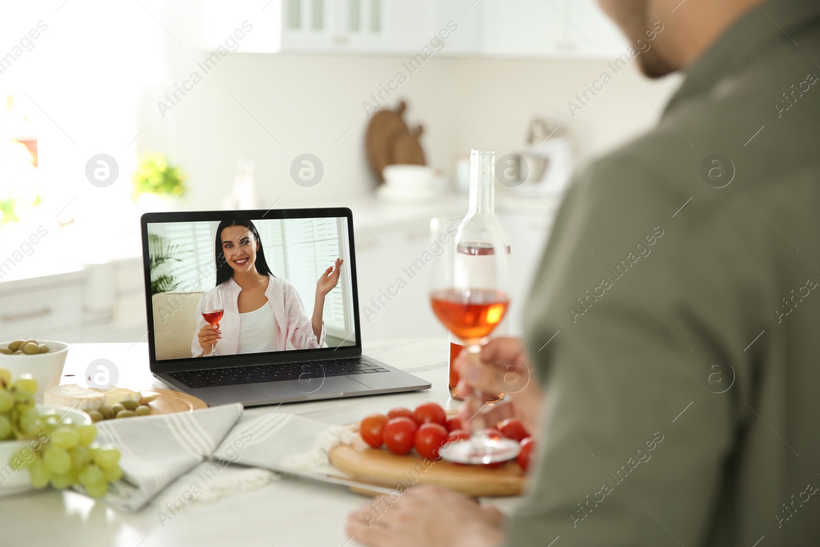 Photo of Friends drinking wine while communicating through online video conference in kitchen. Social distancing during coronavirus pandemic